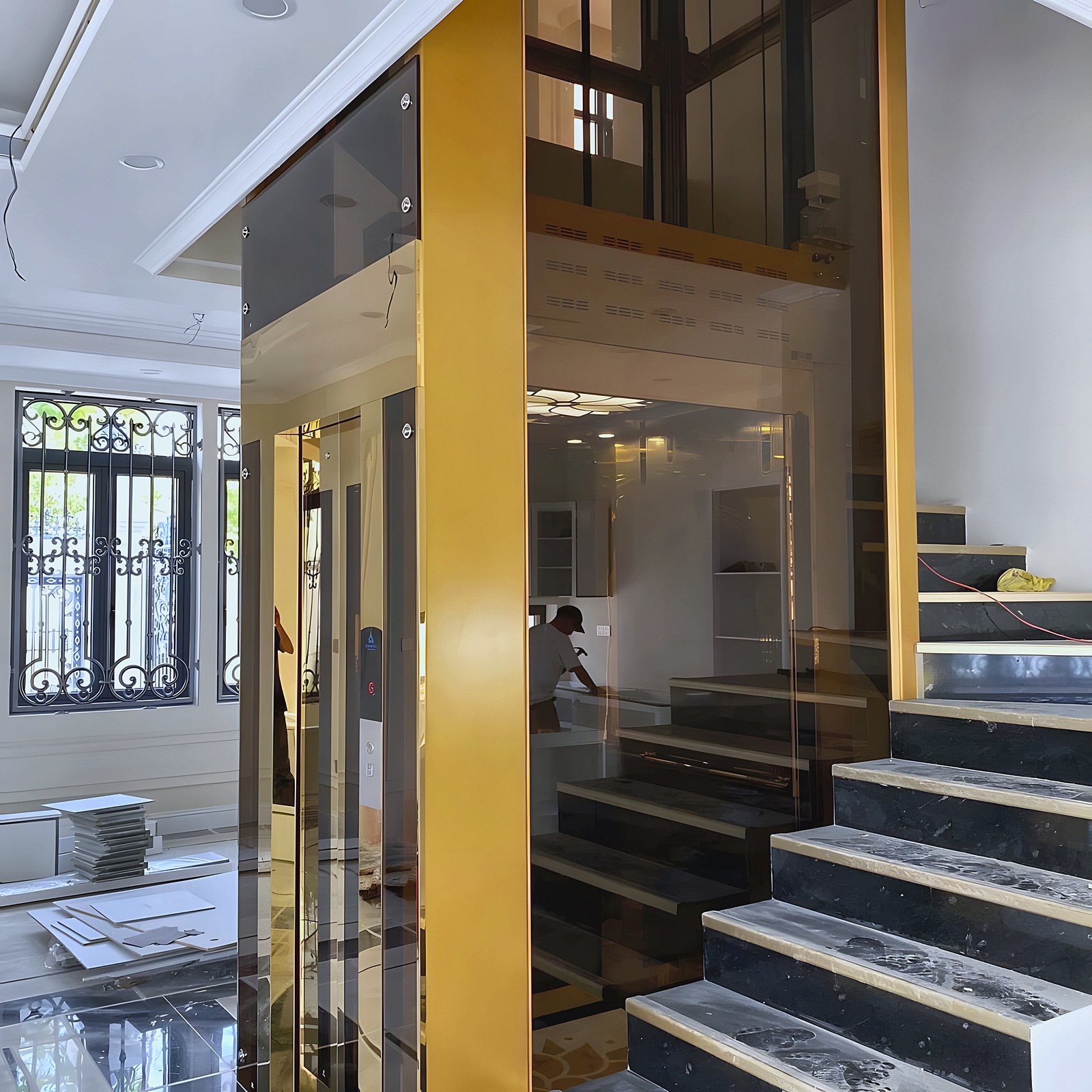 Home lift with a gold frame beside a marble staircase