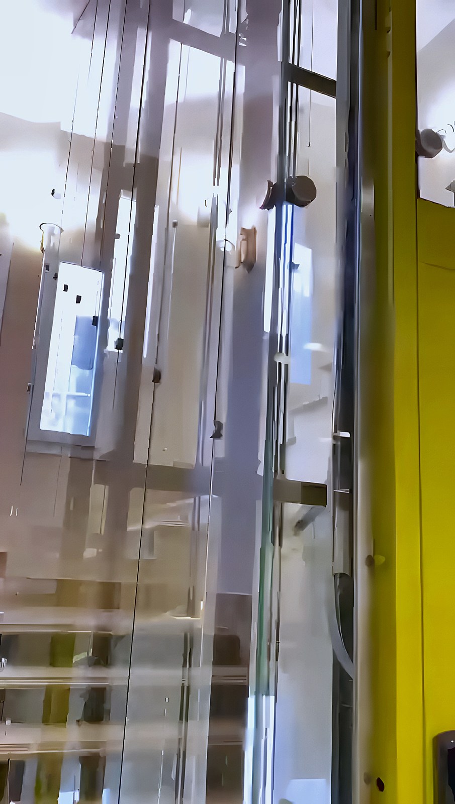 Glass shaft with a yellow frame beside the stairs